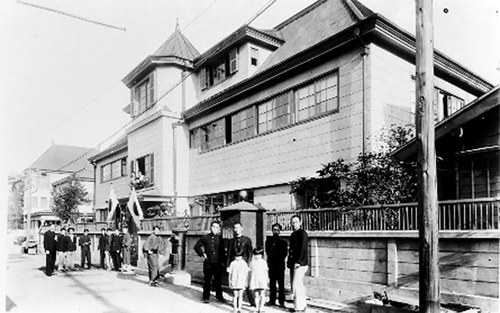 The new building of St. Aloysius Hall, completed in 1932 (demolished in July 1961), with the Jesuits’ residence (now called S.J. House) on the left, and the former Akaboshi Residence on the right. Standing in front of the new building are dormitory residents and children from the neighborhood.